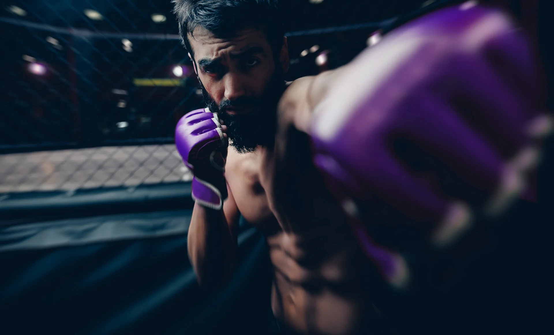 Kampfsportler mit lila Handschuhen im Käfig, Schlagbewegung, Intensität und Schmerz im Profisport